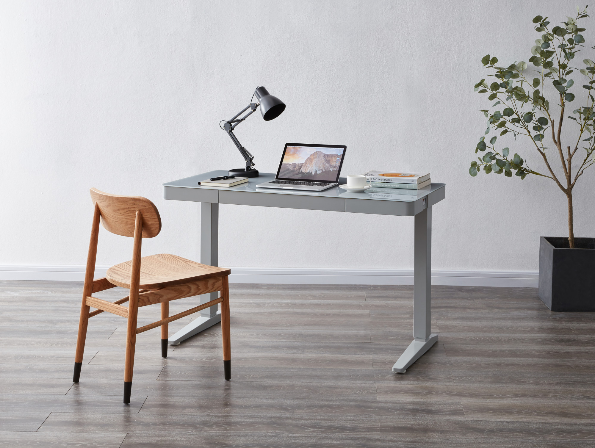 Light grey height adjustable desk with a small wooden oak chair. 