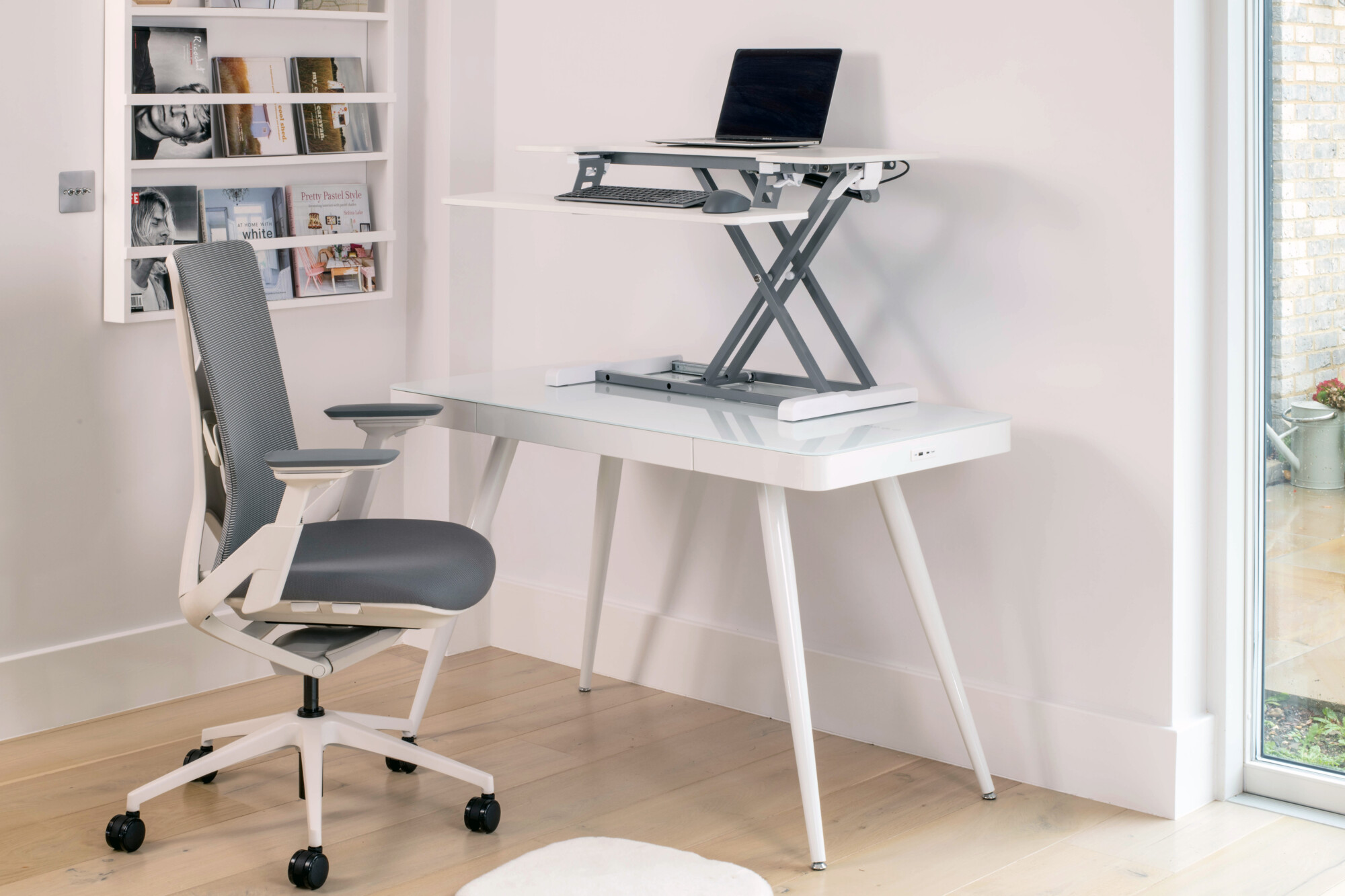 White glass top smart desk with a grey and white mesh ergonomic chair. The smart desk also features a white standing desk converter. 